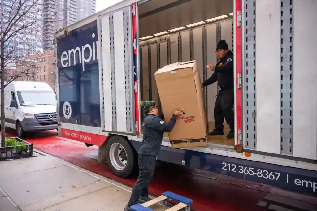 Empire Movers and Storage NYC movers safely lifting a large wardrobe box into a moving truck in New York City.