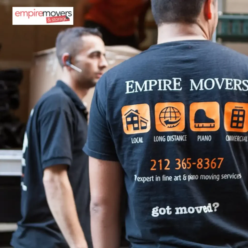 East Side Movers NYC. Two individuals wearing black shirts with the “Empire Movers & Storage” logo are seen from behind, with one shirt displaying white text listing services like local, long-distance, piano, and commercial moving. The shirt also includes a phone number, a tagline reading “got moved?”, and a note about expertise in fine art and piano moving. The other person is partially visible, and the image prominently features the company’s branding in the top left corner.